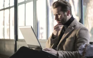 Business man sitting on a bench with his laptop thinking.