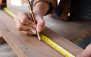 Construction working measuring a block of wood with a ruler and pencil.