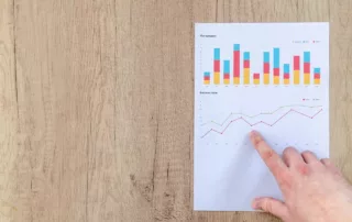 A white man’s hand pointing at a printout of a line graph and bar graph above it.