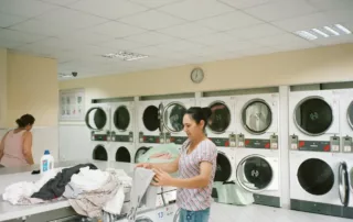 Two women fold their laundry in a laundromat.