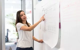 Young Latina business woman points at a graph on a white board.