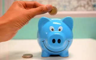 Blue piggy bank with a hand depositing coins into it.