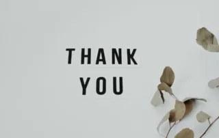 White board with black letters spelling out “Thank you” with some dried leaves to the right.