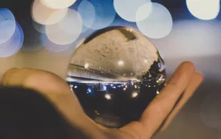 Someone holding a crystal ball along a dark street with lights all around.