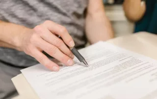 Close up of a person reviewing a contract and pointing with a pen.