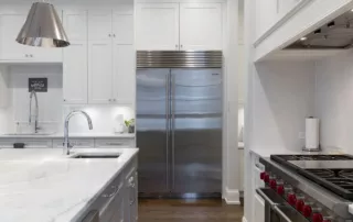 Photo of a stainless steel fridge, sink, and range, in a small modern apartment.